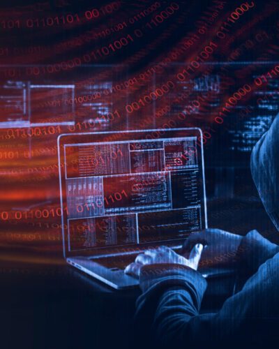 A hooded figure at a laptop surrounded by code &ndash; the everyday reality of cybercrime targeting New Zealand businesses